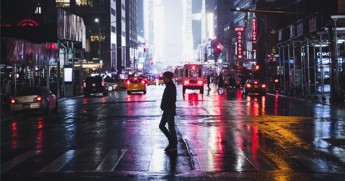 Man crosses busy New York city street at night, wet rainy asphalt, city lights and car tail lights in background 85