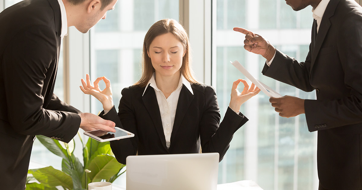 Woman holds hands to either side of her head in yoga meditation pose, one man on either side of her tries to get her attention. all three is business attire, office setting