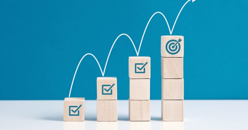 Wooden block towers are lined up from shortest to tallest. Checkmarks top the first three, and a bullseye is on the last one.