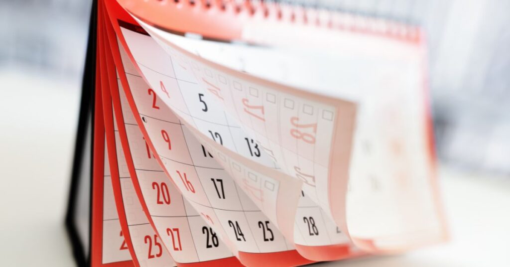 The pages of a spiral-bound desk calendar are flipping upward from the bottom left corner. The calendar is red, black, and white.