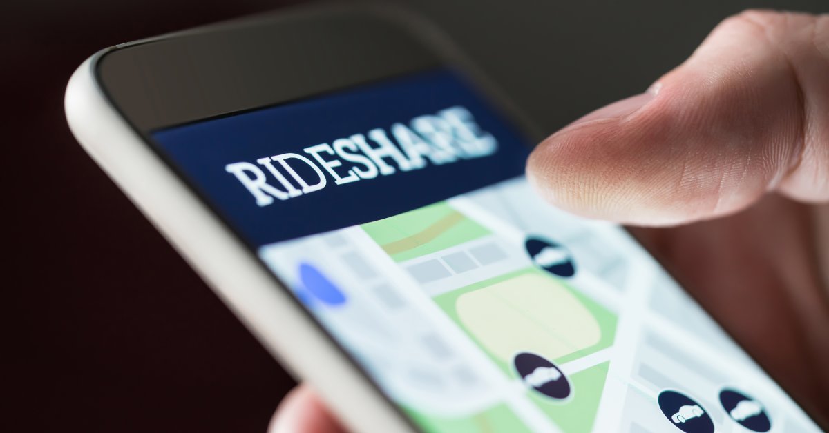 Close-up of a phone screen with the word "rideshare" and a map with car icons. A person's thumb hovers over the screen.