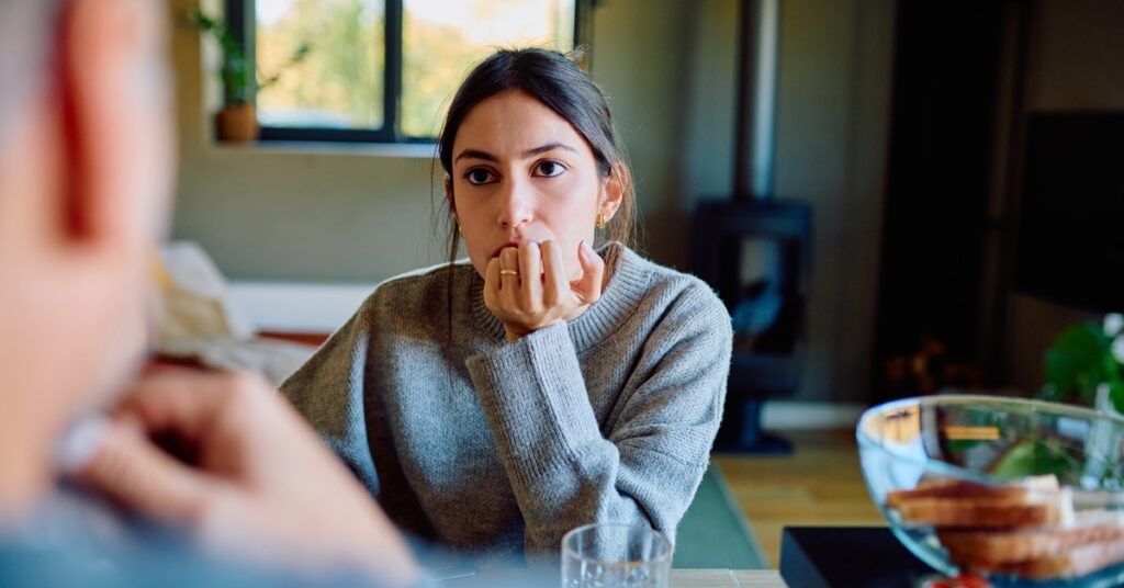 A woman in a conversation watches the person in front of her. Her chin rests on her hand, which obscures her mouth.