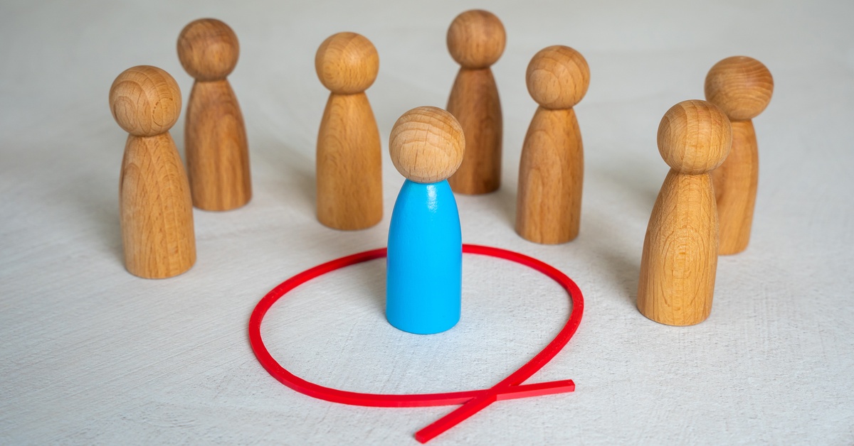 Wooden human figurines sit on the table with a blue-painted figurine sitting inside a red circle as a boundary.