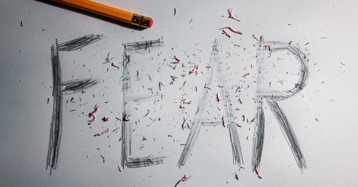 The word "FEAR" is in block letters next to a yellow pencil. The word is partially erased and covered in eraser debris.