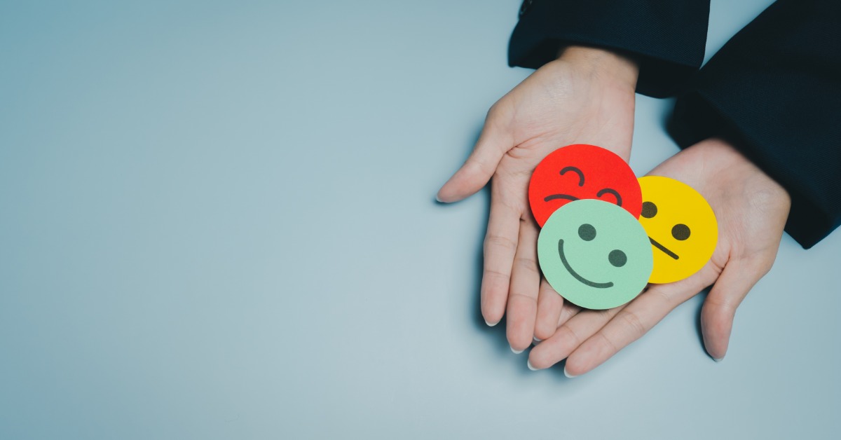 A person holds colored paper circles that have different facial expressions. The green circle has a smiley face.