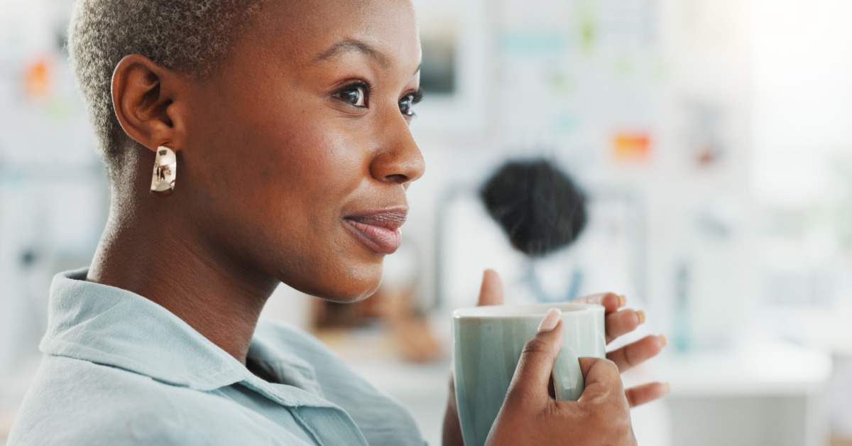 Close-up of a woman holding a light blue mug with both hands. She looks to the side and smiles slightly.
