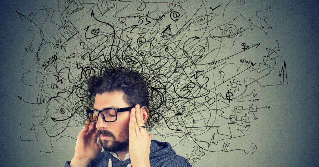 A man holds both hands to the sides of his head. A large cluster of black doodles appears behind and above his head.